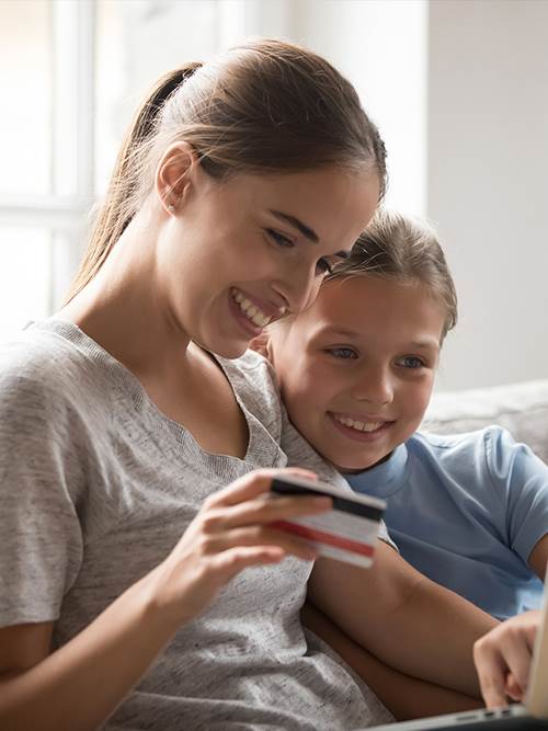 woman and young girl at home on laptop mom teaching daughter to save using common cents program